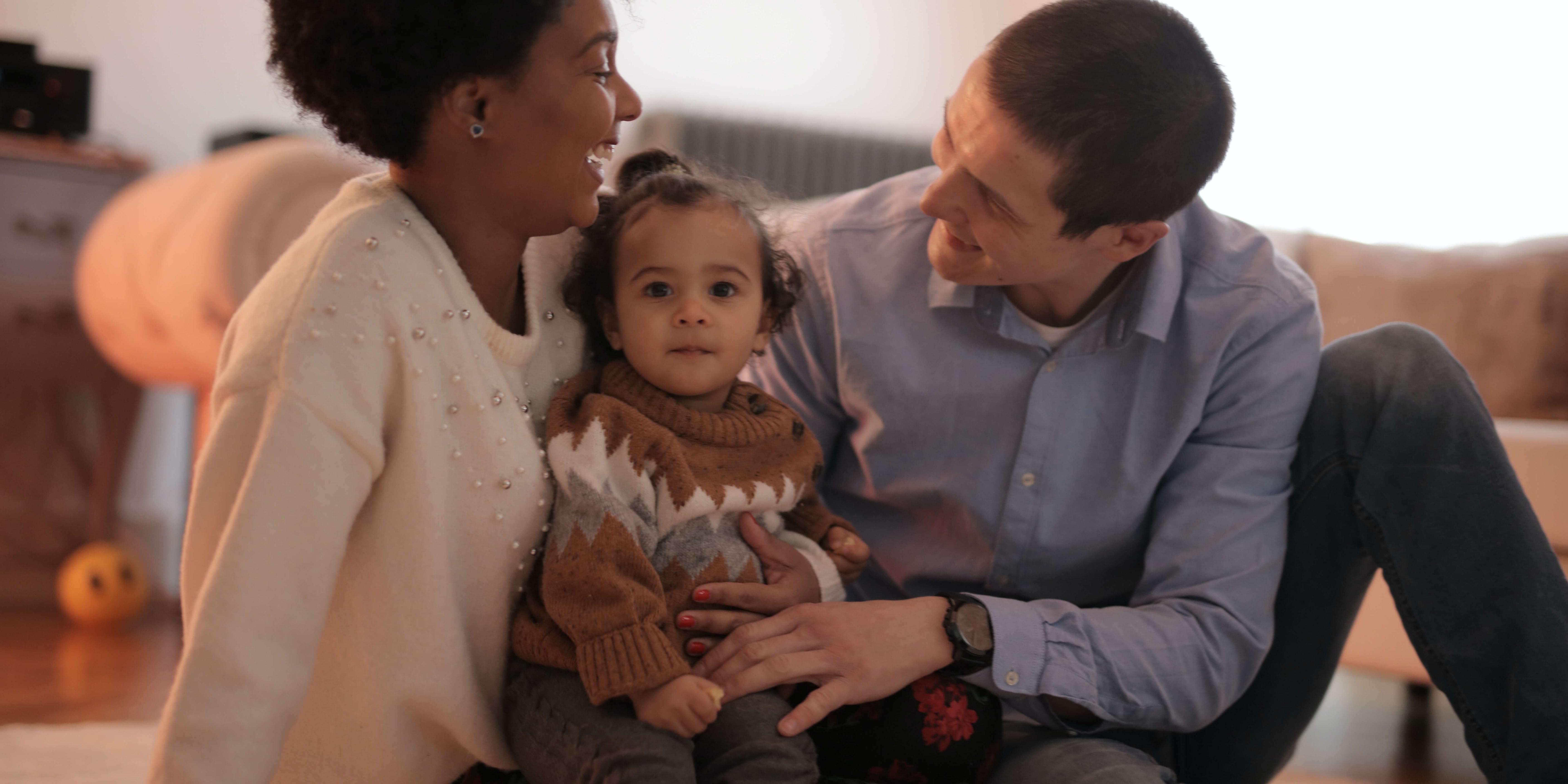 Man and woman sitting on the floor with toddler, smiling and laughing