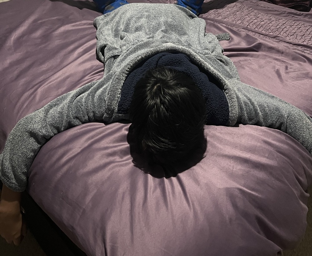 Someone lies face-down on a bed with arms outstretched.