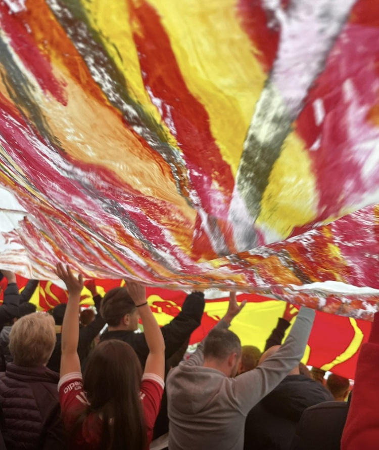 People raise their hands to hold up a red and yellow veil above them.